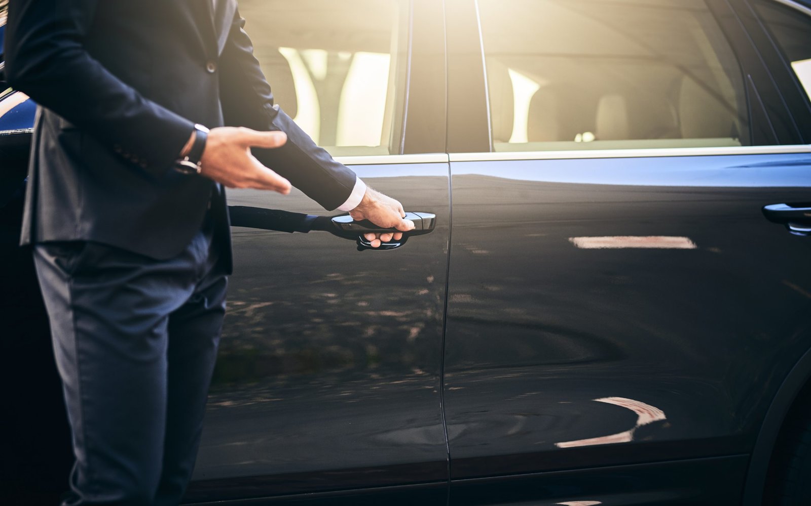 Fly Limo chauffeur opening the rear door of a luxury sedan at sunset